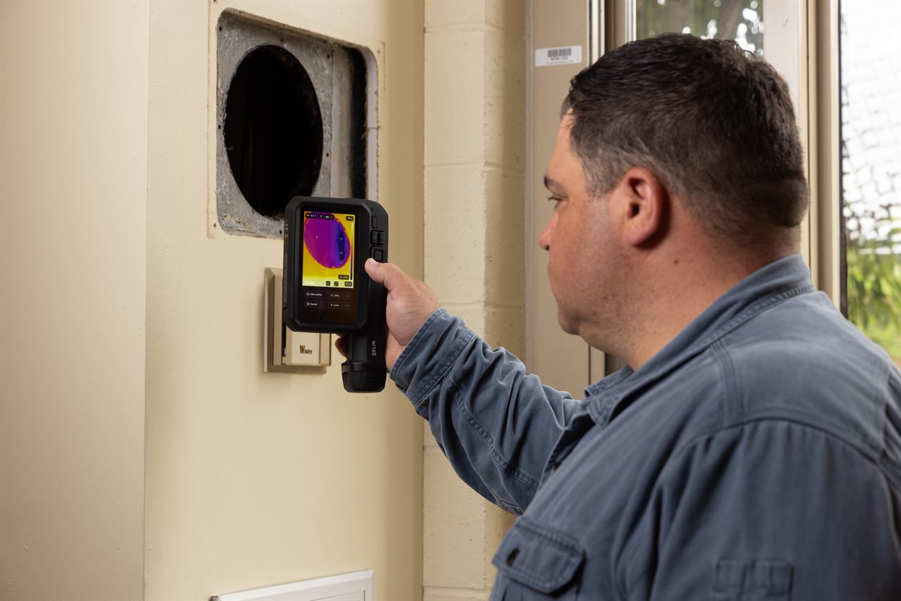 Technician performing an HVAC and mechanical thermal inspection with a FLIR camera.