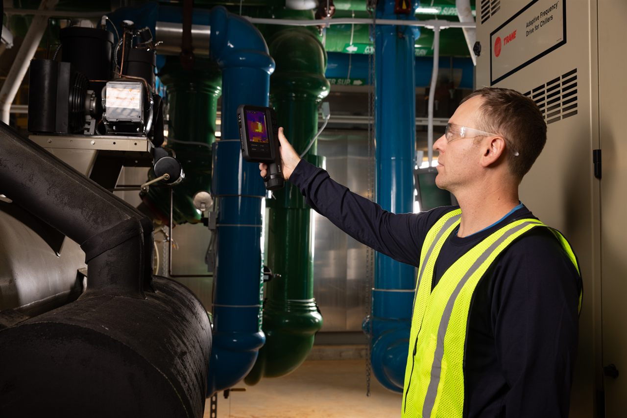 Technician carrying out a thermal inspection inside an industrial plant with a FLIR camera.