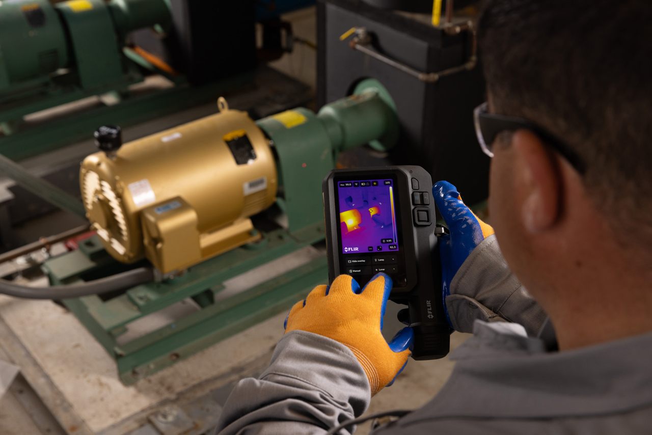 Gloved technician scanning an electric motor with a FLIR thermal camera, a thermal readout on the screen.