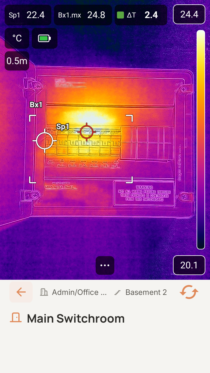 SwitchReport live capture screen on the FLIR i34: a thermal image of a switchboard with a crosshair on the automatically detected hot spot and a ΔT readout.